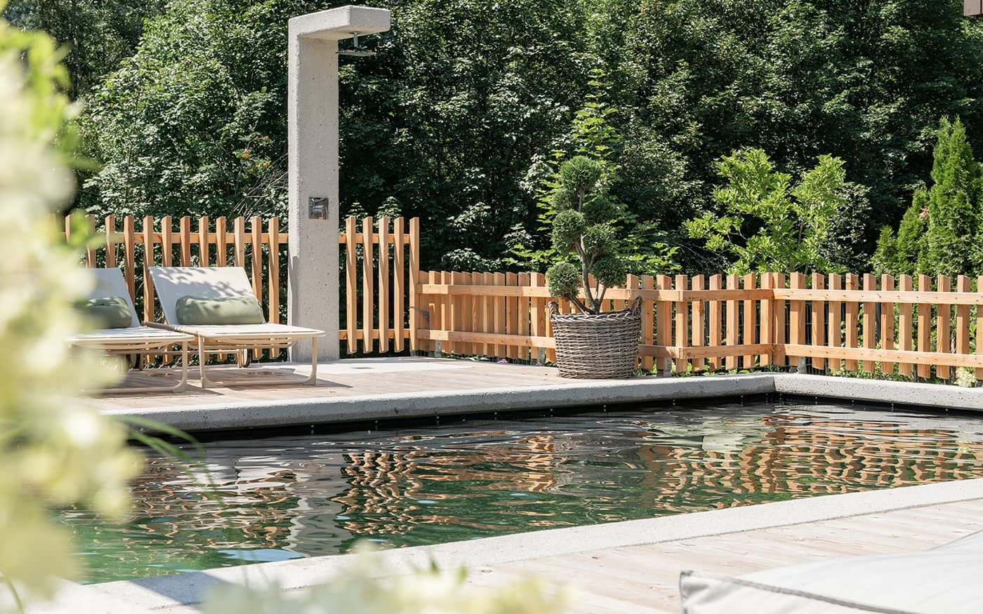 Liegest&uuml;hle und Dusche am Pool mit gr&uuml;nem Hintergrund und Holzzaun