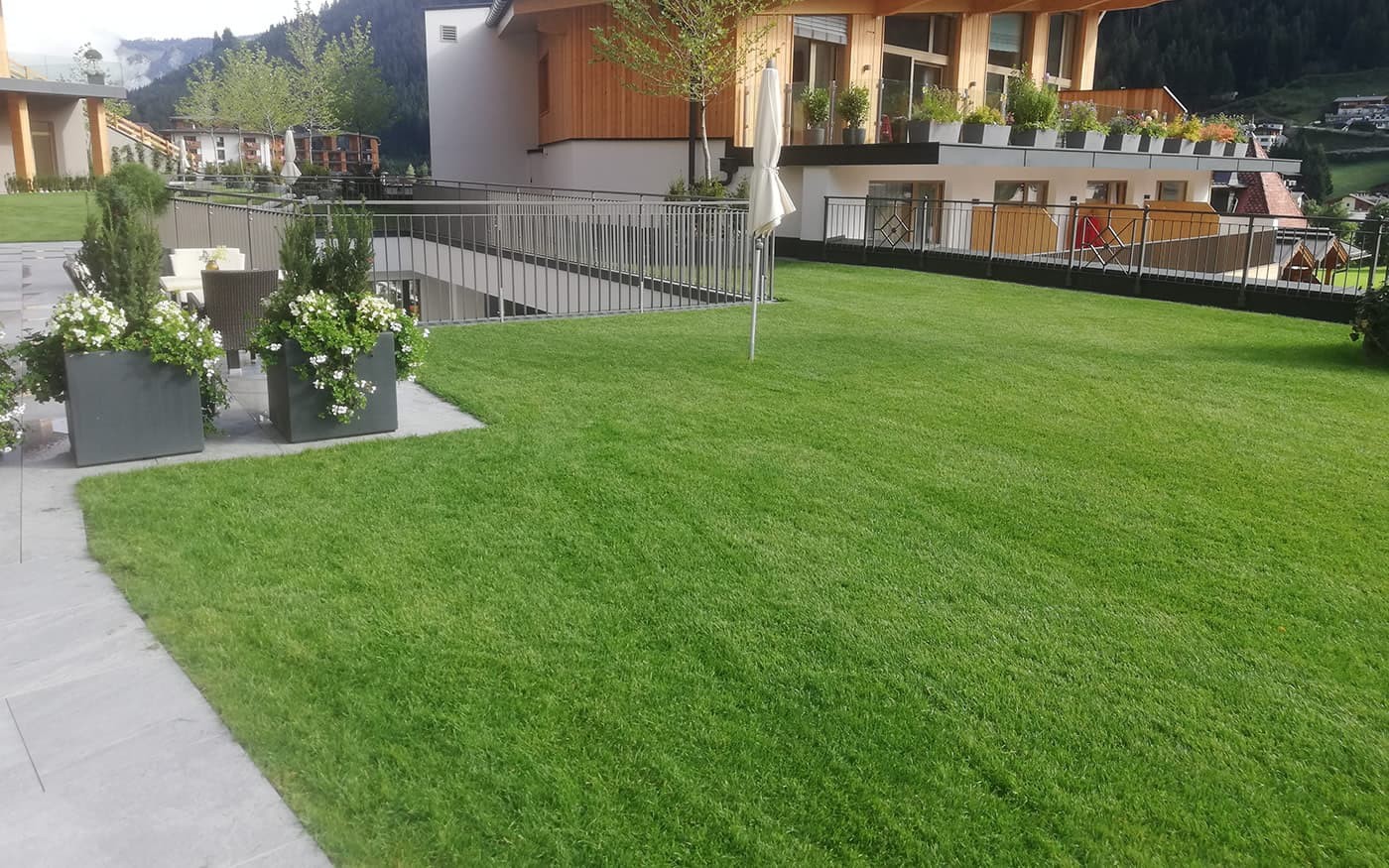 Gr&uuml;ner Rasen vor einem modernen Geb&auml;ude mit Balkon und Blumenk&auml;sten