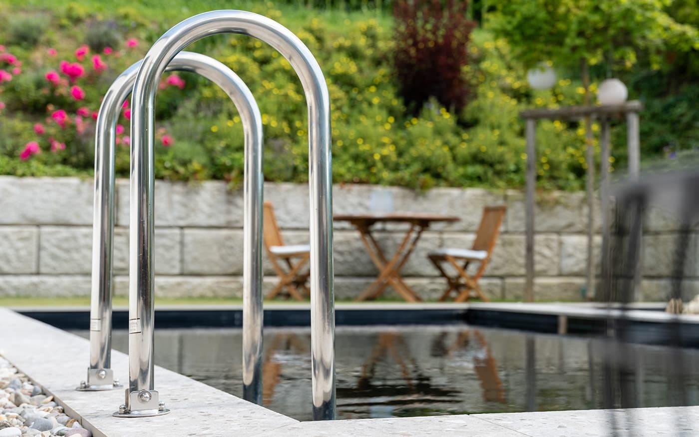 Poolleiter mit Blick auf Tisch und St&uuml;hle in einem bl&uuml;henden Garten
