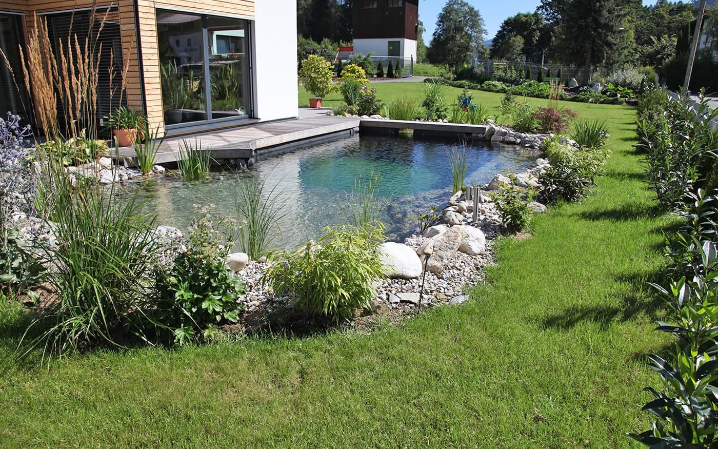 Moderner Garten mit kleinem Teich und &uuml;ppiger Vegetation, neben einem Holzhaus