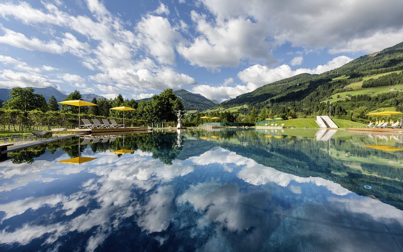 Ein klarer Pool spiegelt den Himmel und Berglandschaft wider, umgeben von gr&uuml;nen Wiesen