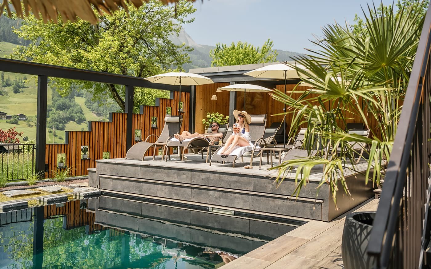 Personen entspannen sich auf Liegest&uuml;hlen neben einem Pool unter Sonnenschirmen