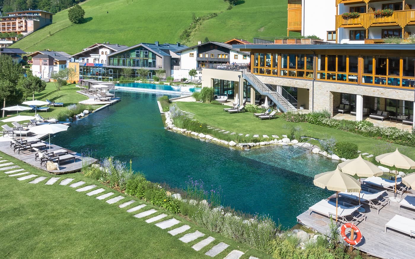 Ein Hotel mit nat&uuml;rlichem Schwimmteich und Liegen in einer gr&uuml;nen, h&uuml;geligen Umgebung